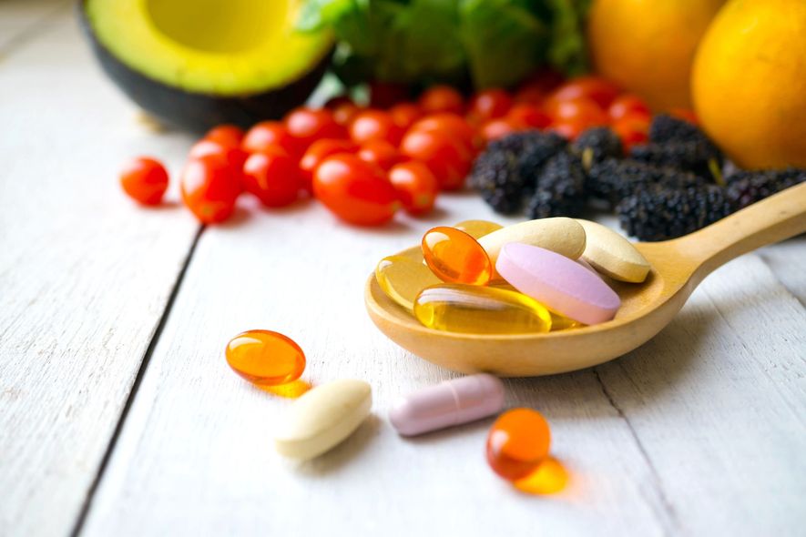 A wooden spoon filled with vitamins and vegetables on a table.