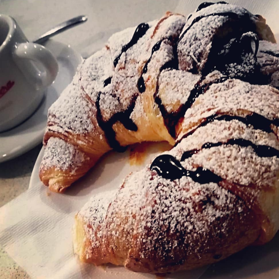 Un croissant ricoperto di zucchero a velo accanto a una tazza di caffè