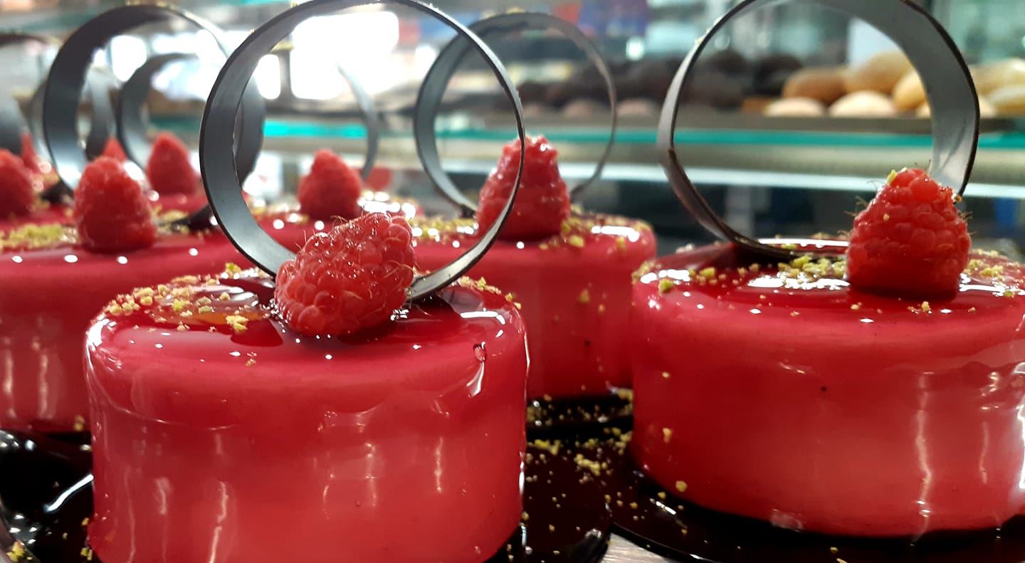 Un primo piano di una vetrina di dolci con lamponi sopra.