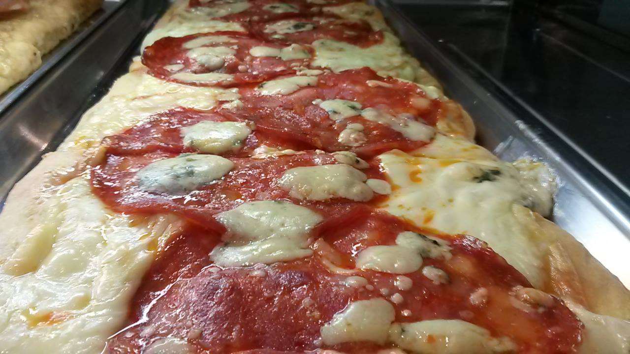 Una pizza lunga con salame piccante e formaggio è appoggiata su un vassoio.