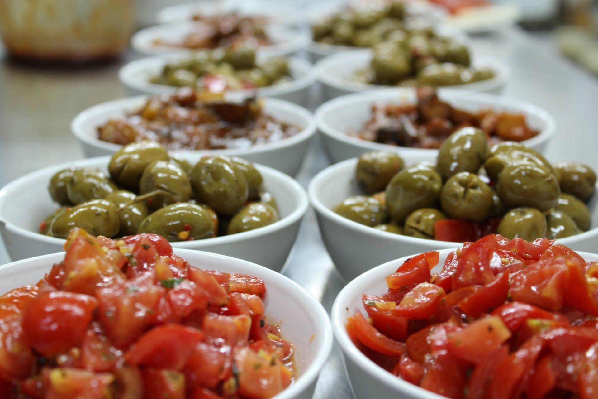Una fila di ciotole piene di diversi tipi di cibo per aperitivo, tra cui olive e pomodori.