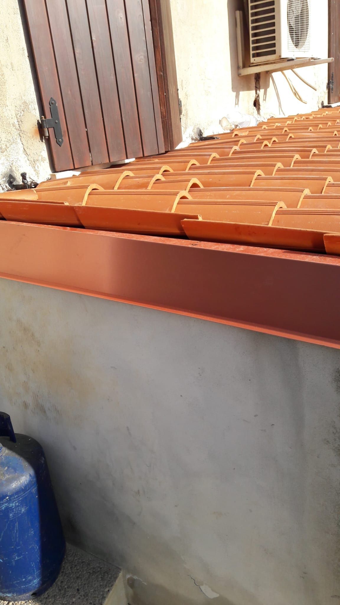 Un tetto di tegole rosse è appoggiato su un muro di cemento accanto a una finestra.