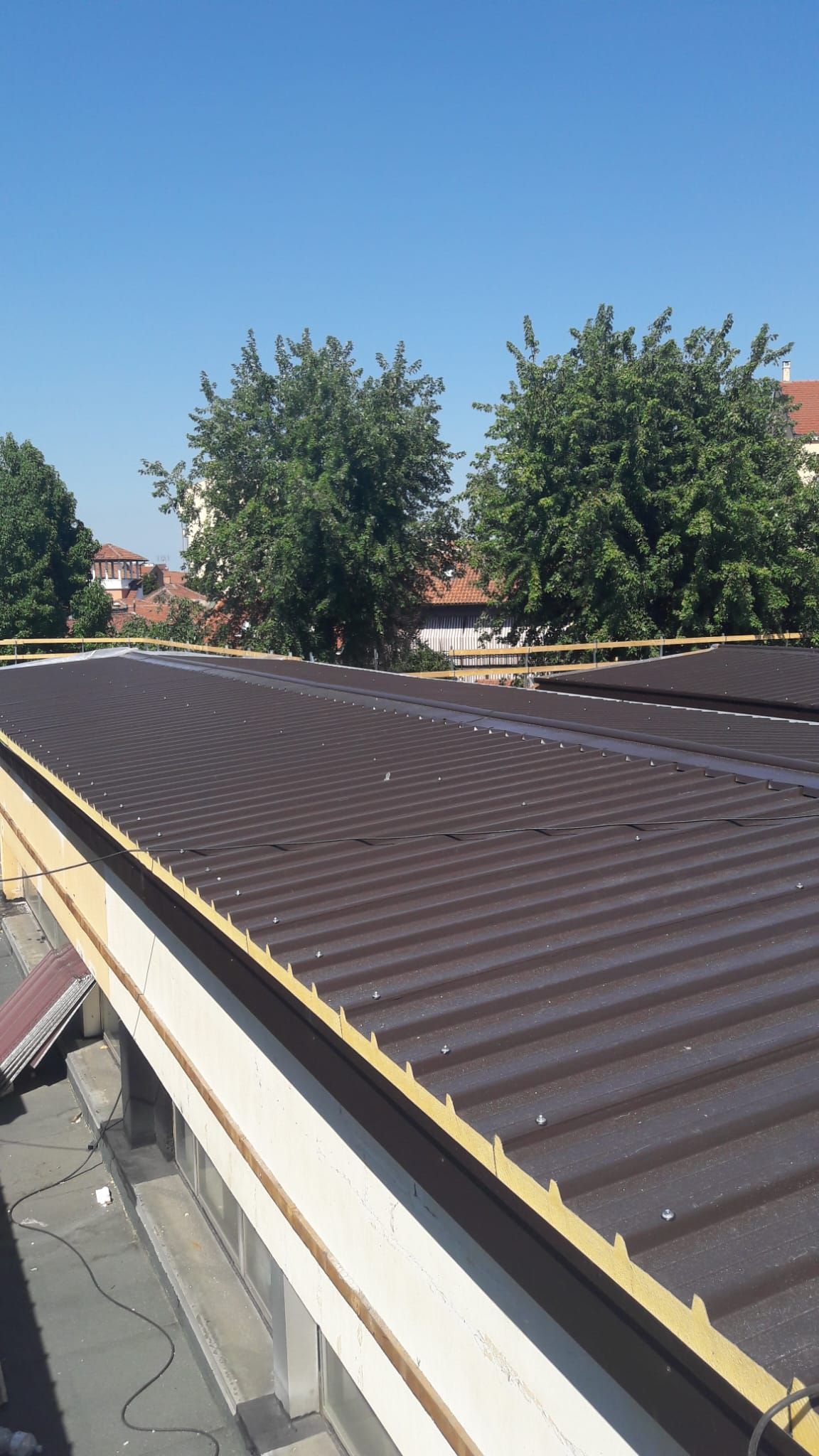 Si sta costruendo un tetto in una giornata di sole, con alberi sullo sfondo.