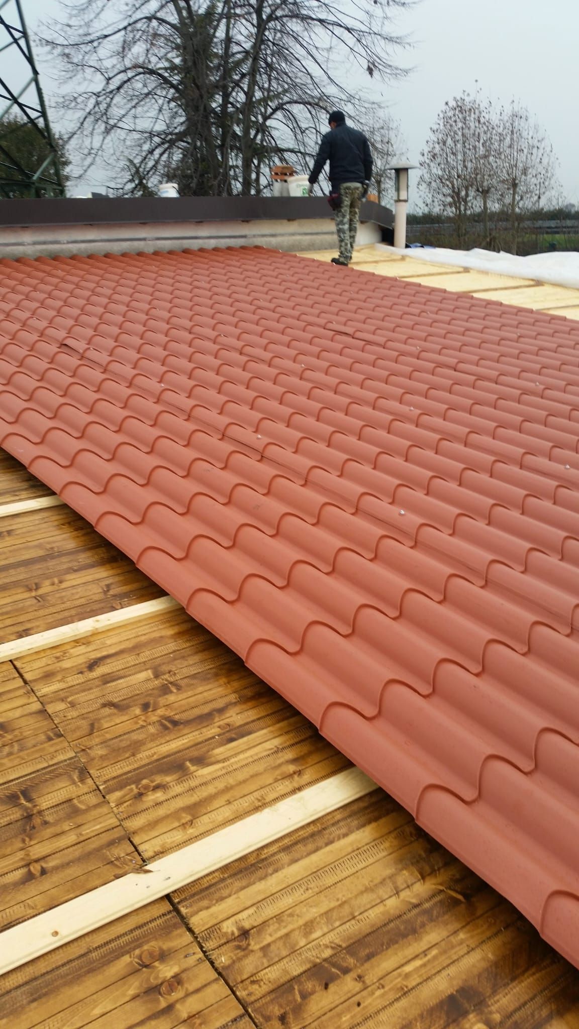 Un uomo è in piedi in cima a un tetto di legno con tegole rosse.