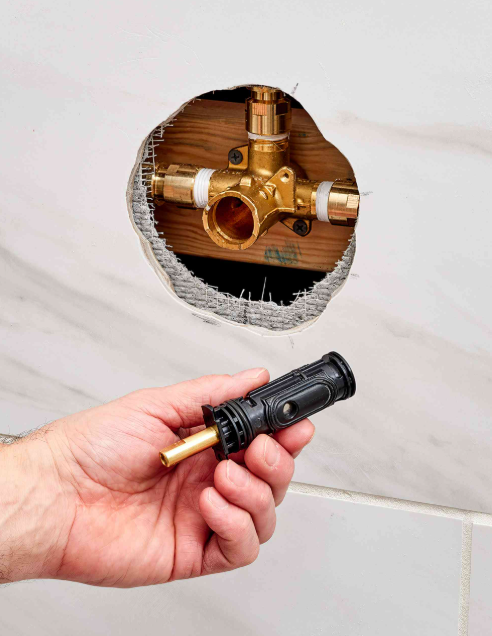 A person is holding a piece of metal in their hand in front of a hole in a wall.