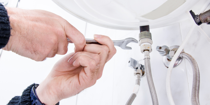 A man is fixing a sink with a wrench.