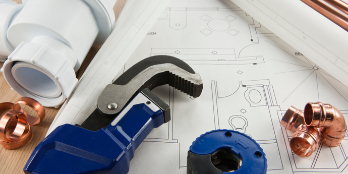 A plumbing wrench is sitting on top of a blueprint on a wooden table.
