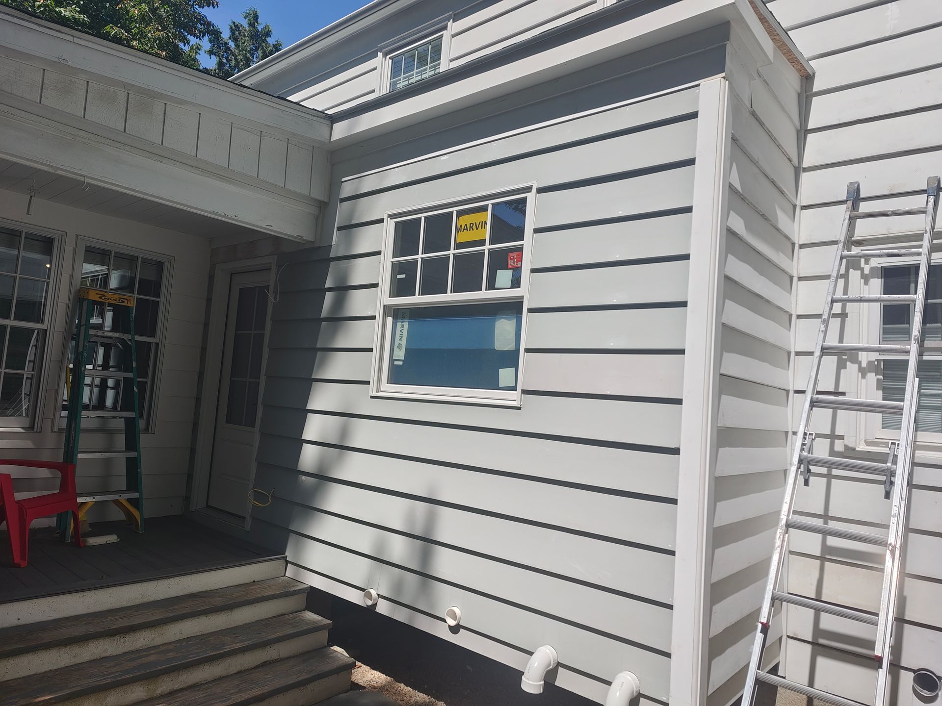 A white house with a window and a ladder on the side of it.