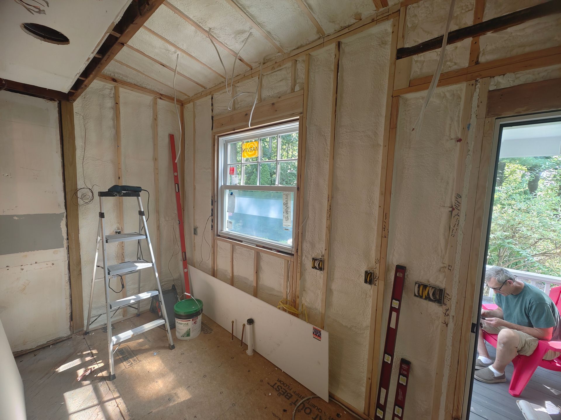 A man is sitting in a red chair in a room with a ladder and a window.