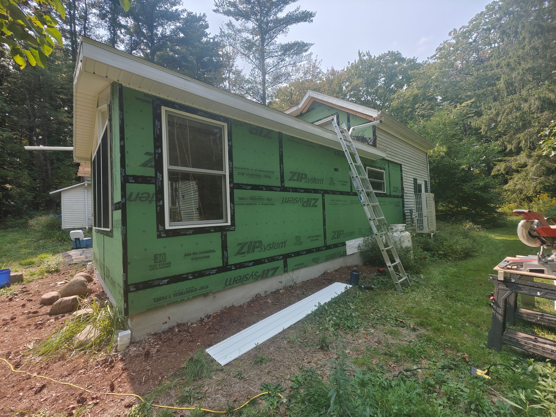 A house is being remodeled with green siding and a ladder.