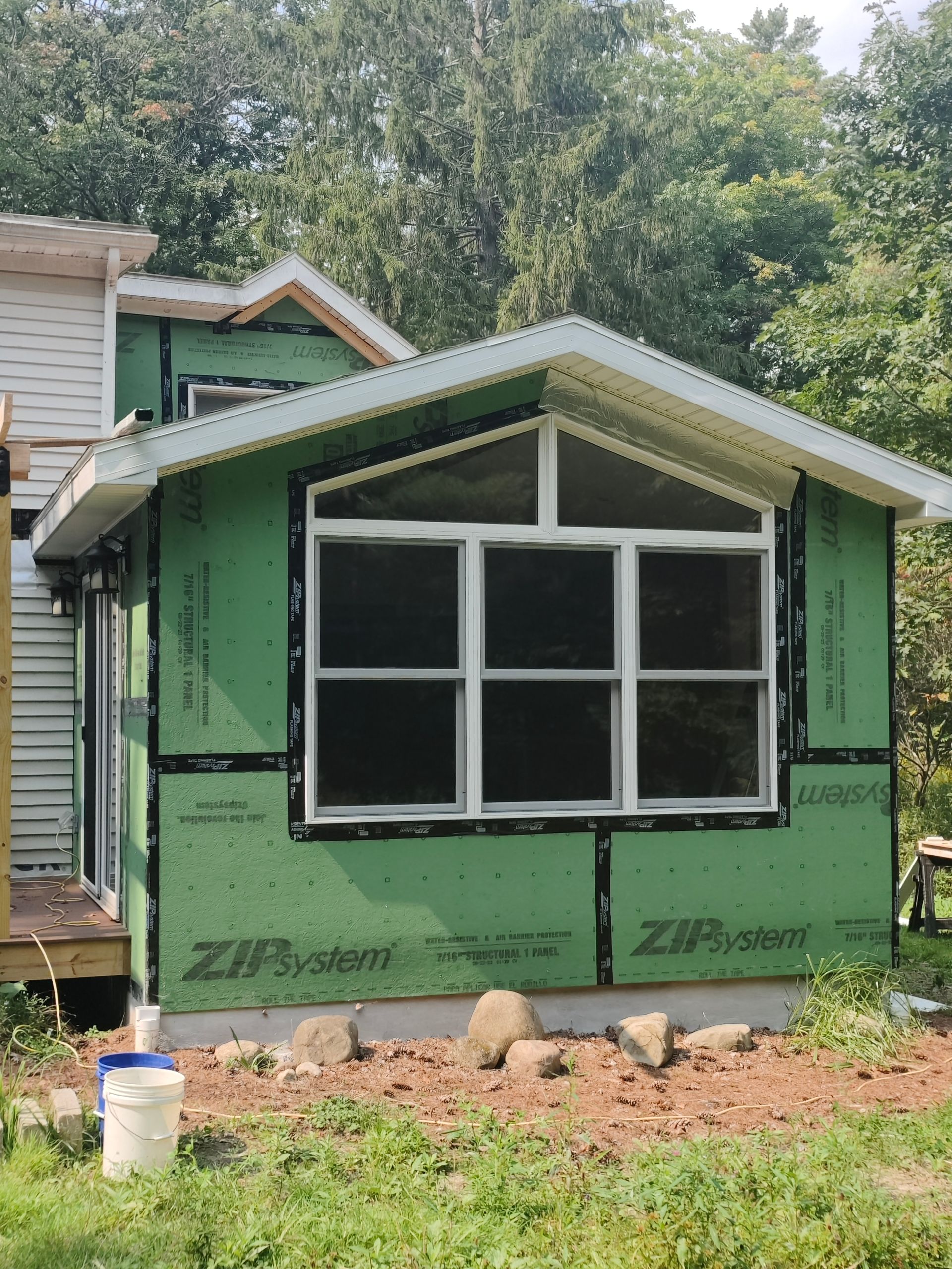 A small house is being built with green siding and a window.
