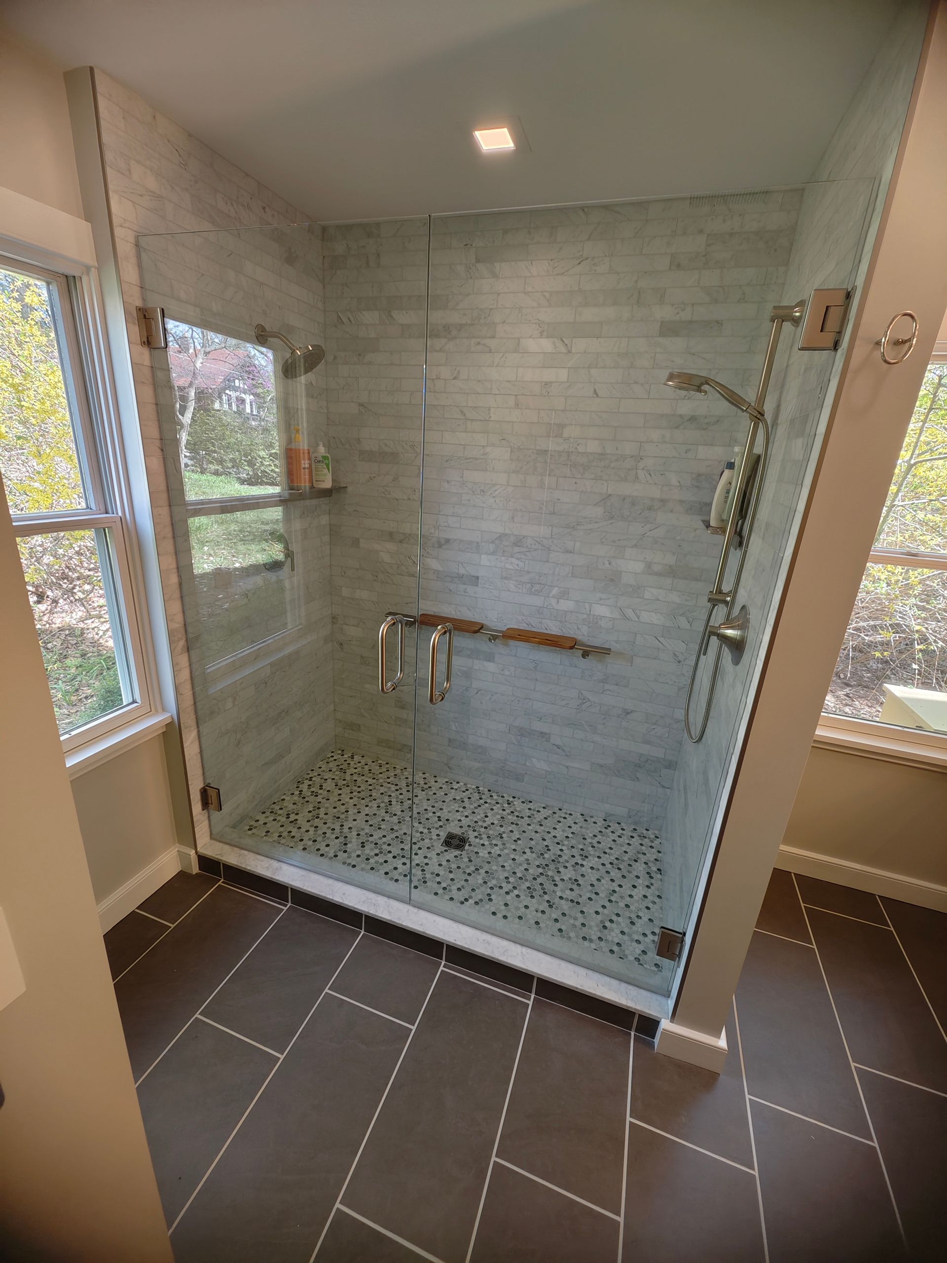 A bathroom with a walk in shower with a glass door and a window.