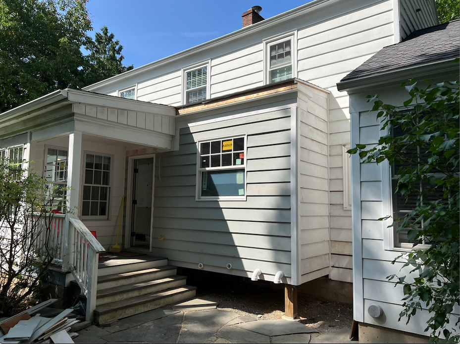 A white house with a porch and stairs is being remodeled.