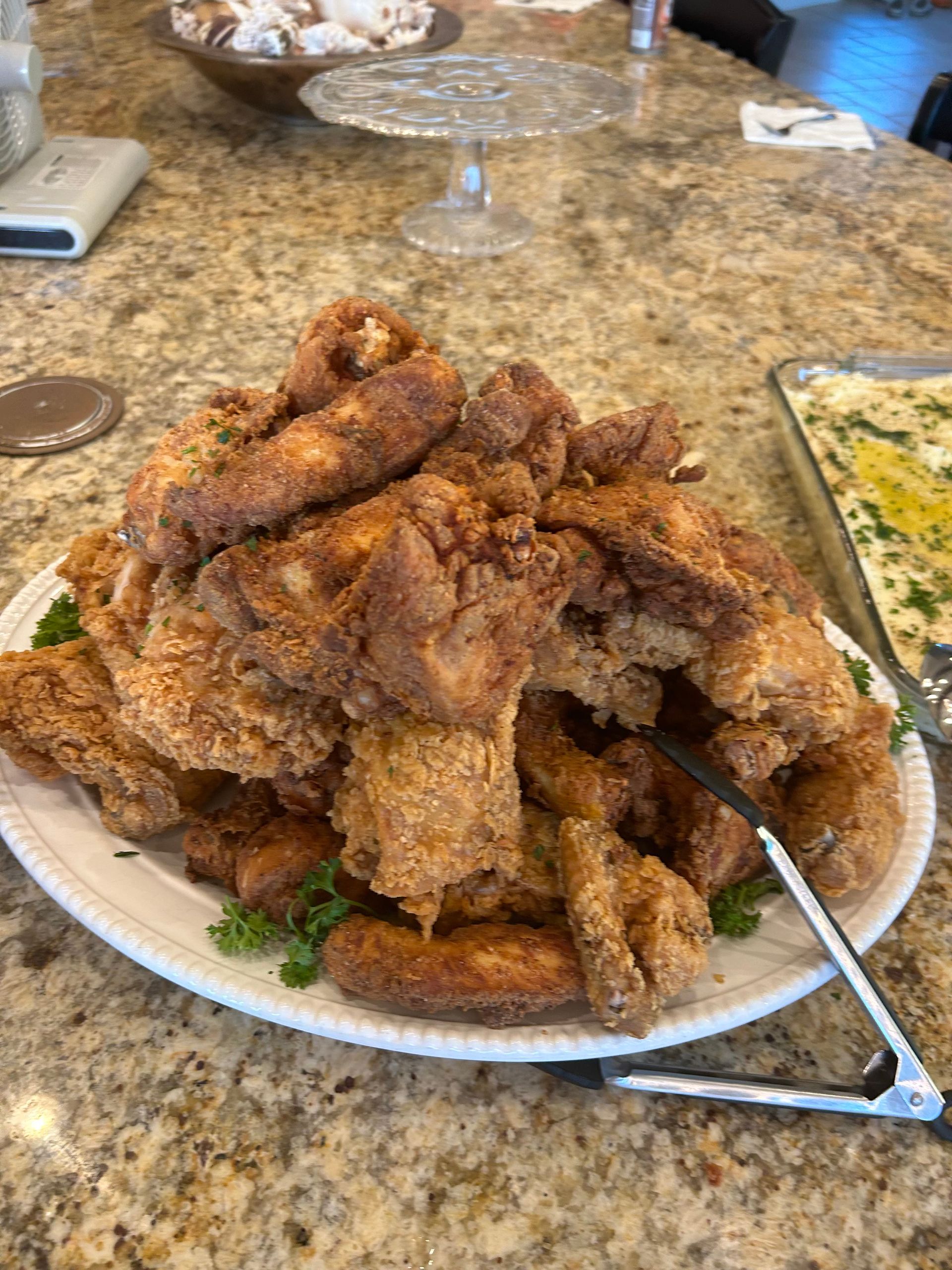 a plate of fried chicken and potatoes on a table with tongs . — Mary Esther, FL — Bella Donna Catering