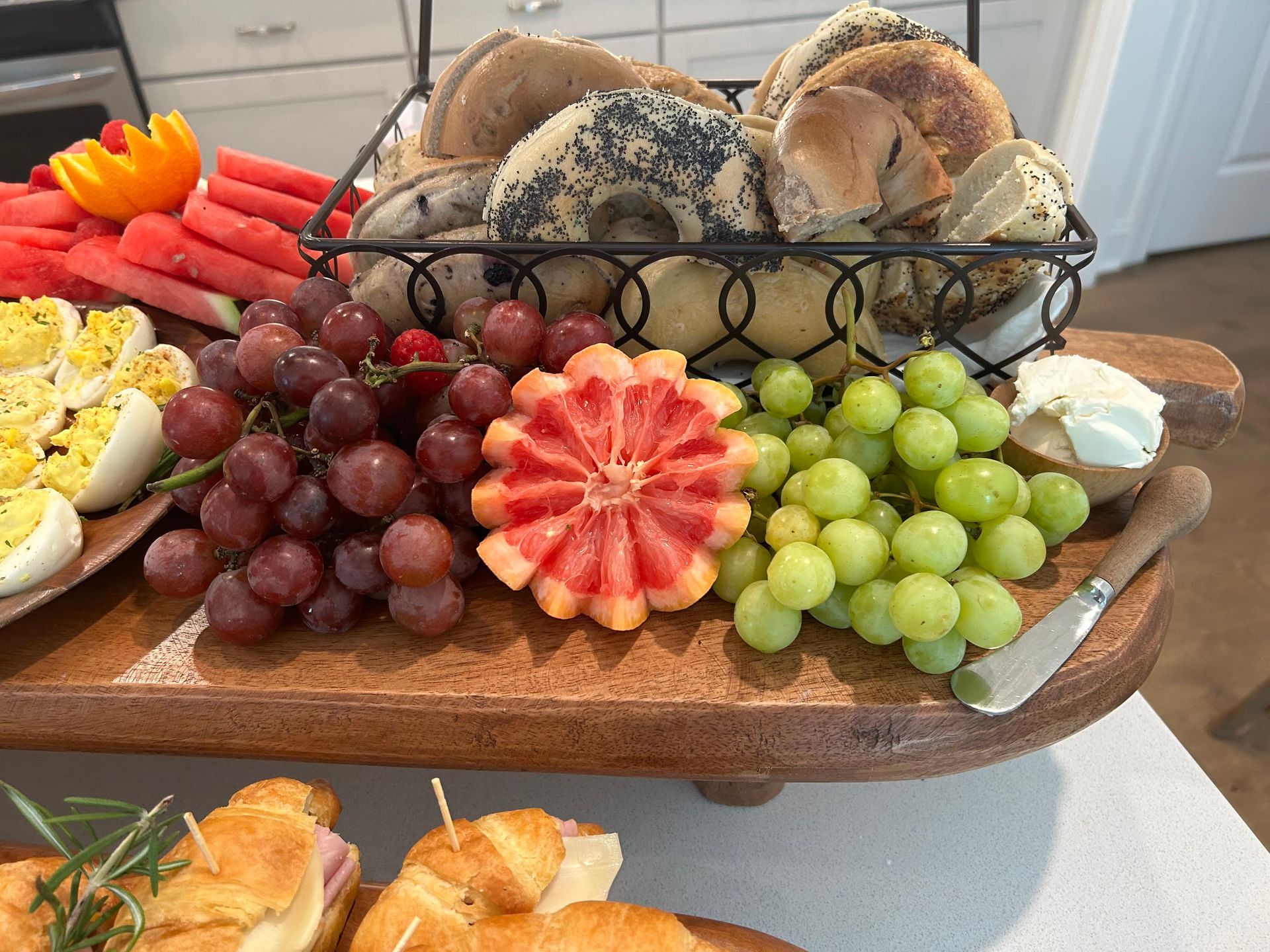 a wooden cutting board with a basket of fruit and bread on it . — Mary Esther, FL — Bella Donna Catering