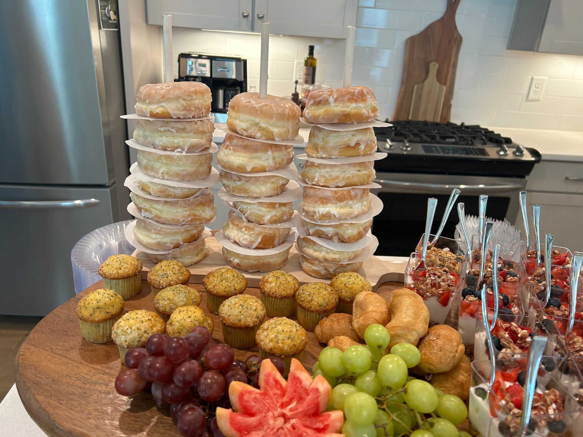 a wooden cutting board topped with donuts , muffins , grapes and fruit . — Mary Esther, FL — Bella Donna Catering