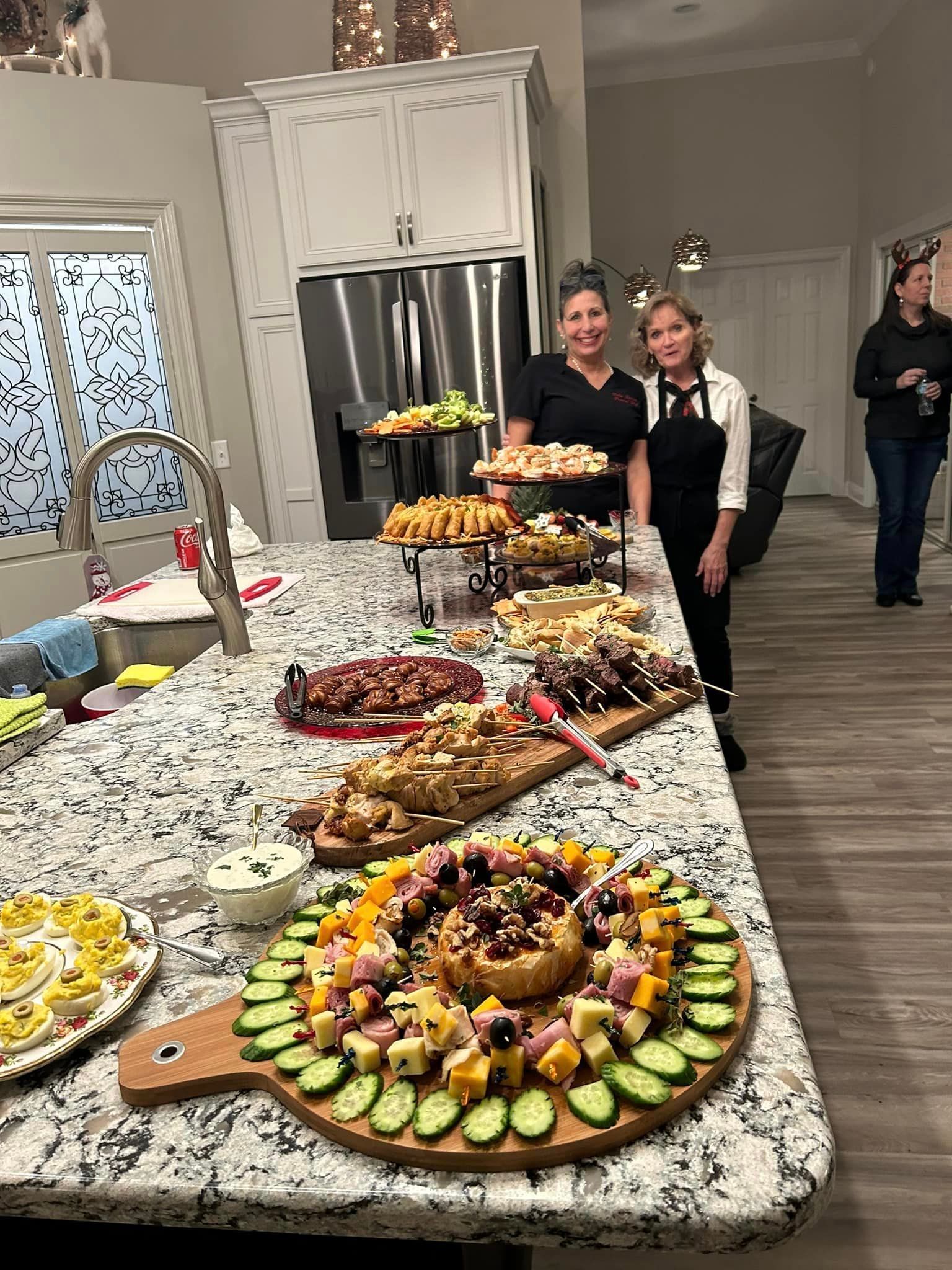 two women are standing in front of a buffet table filled with food . — Mary Esther, FL — Bella Donna Catering