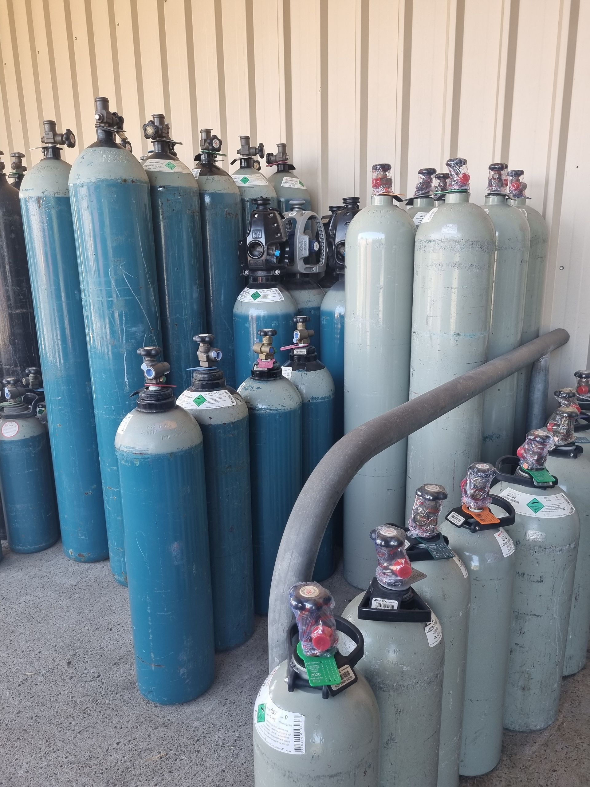 Rows of blue, white, and gray gas cylinders stored in a warehouse-like space