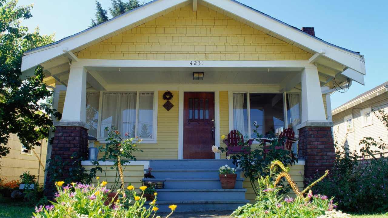 A yellow house with a porch and flowers in front.