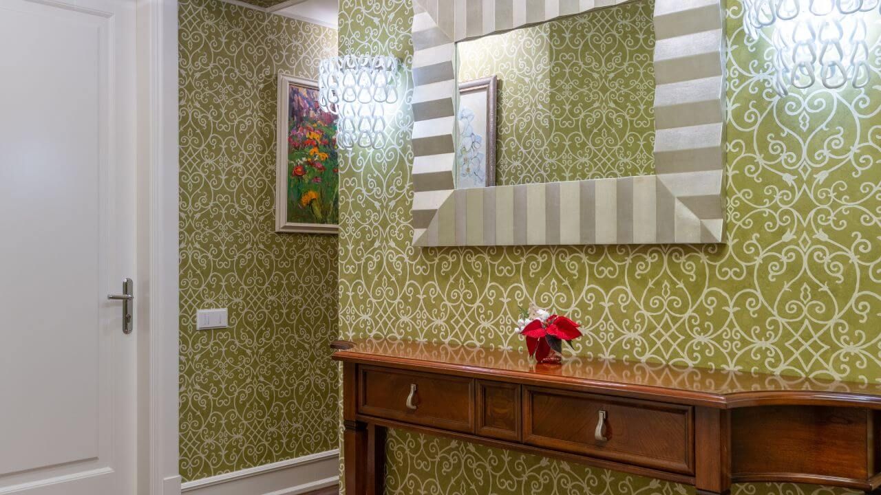 A hallway with green wallpaper and a mirror reflecting the surroundings.