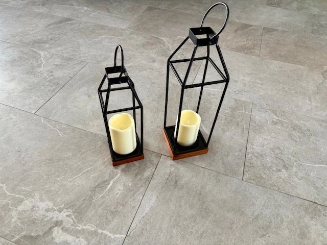 Two black metal lanterns with cream-colored candles on a tiled floor.