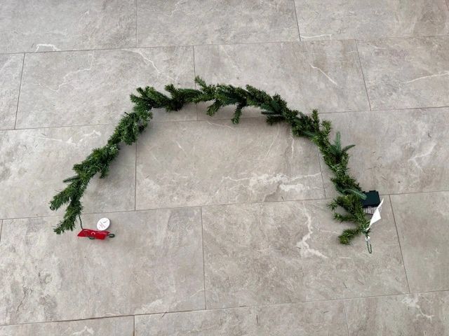 Green garland on a light gray tiled floor. Tags hang from the garland.