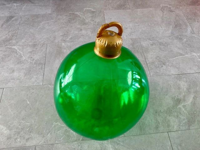 Large, green Christmas ornament with gold top on a gray tiled surface.