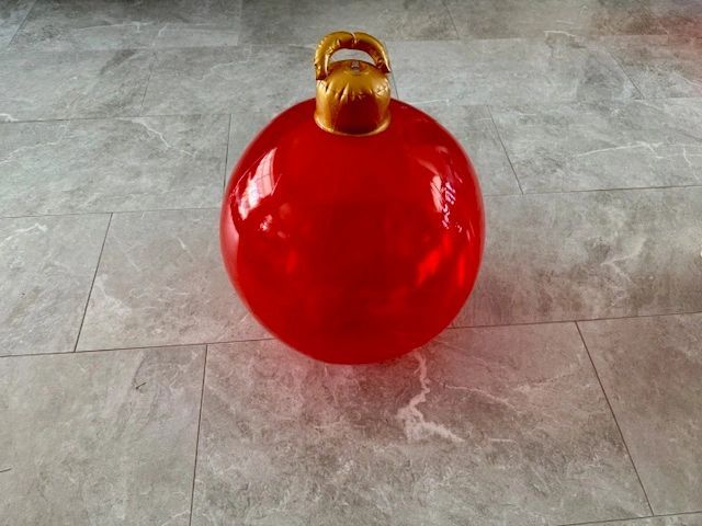 Large red Christmas ornament with gold cap, on a gray tile floor.