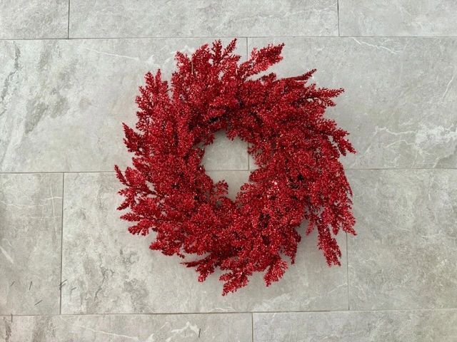 Red, glittery wreath hanging on a gray-tiled wall.