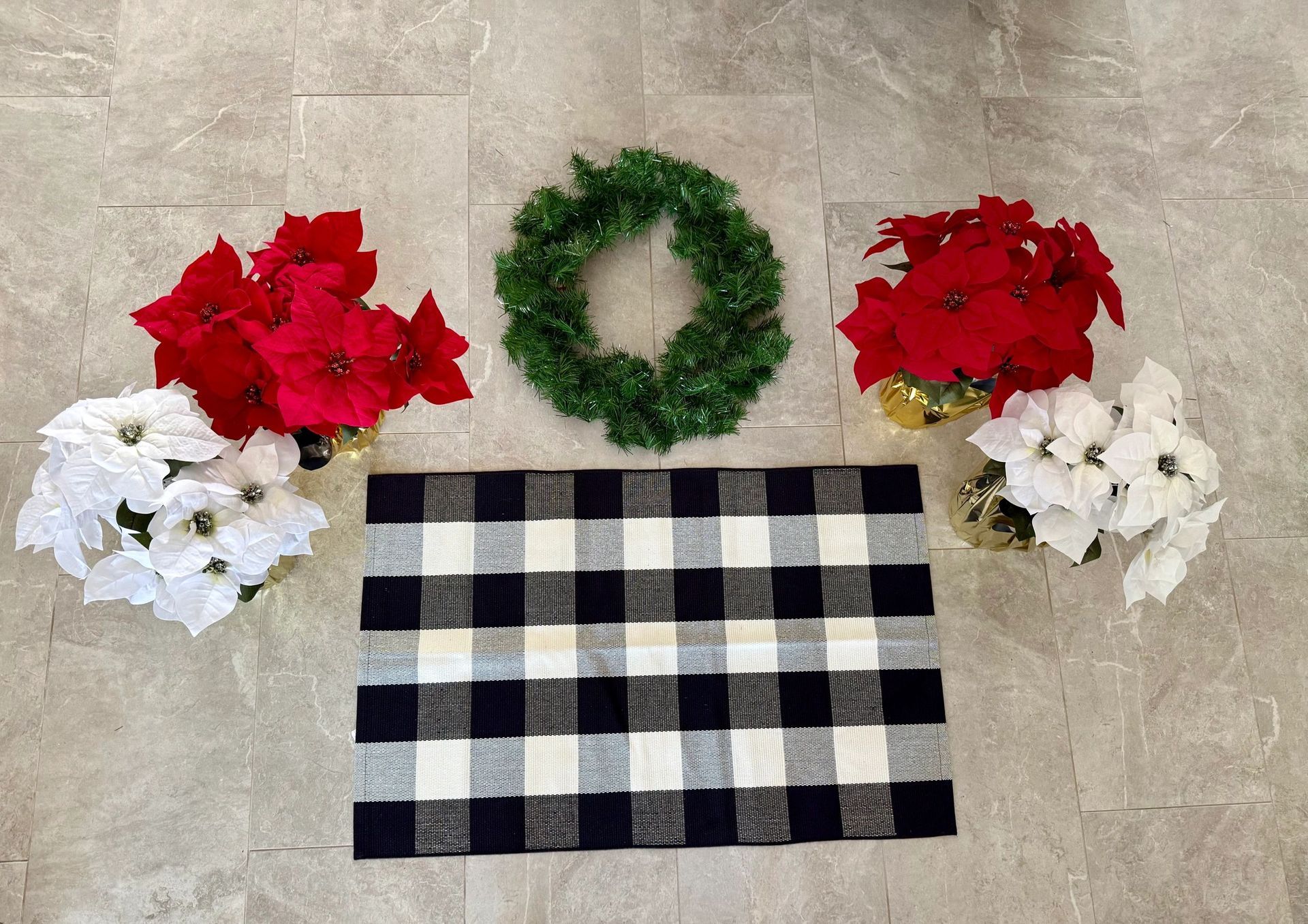 Poinsettias, a green wreath, and a black and white checkered mat on a stone floor.