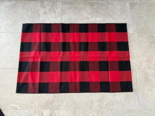 Red and black buffalo plaid rug on a light-colored tile floor.