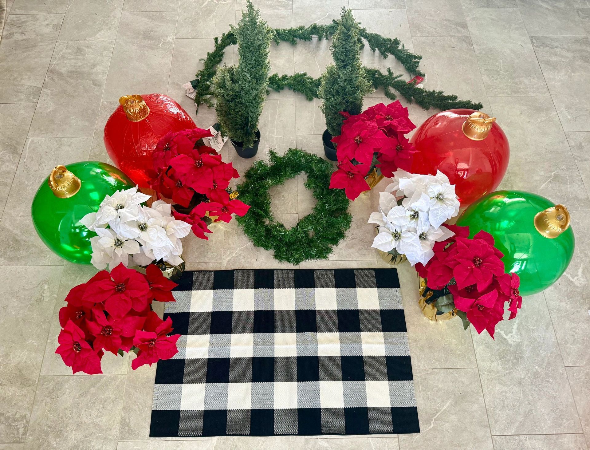 Christmas decorations: red, green ornaments, poinsettias, wreath, garland, checkered rug, on floor.