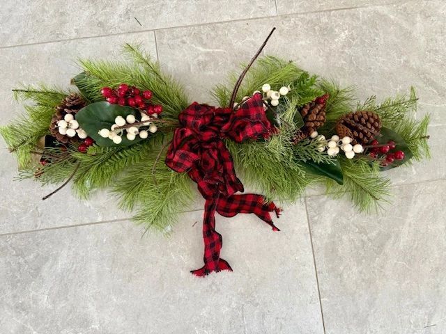 Christmas table centerpiece with red plaid bow, greenery, berries, and pinecones.