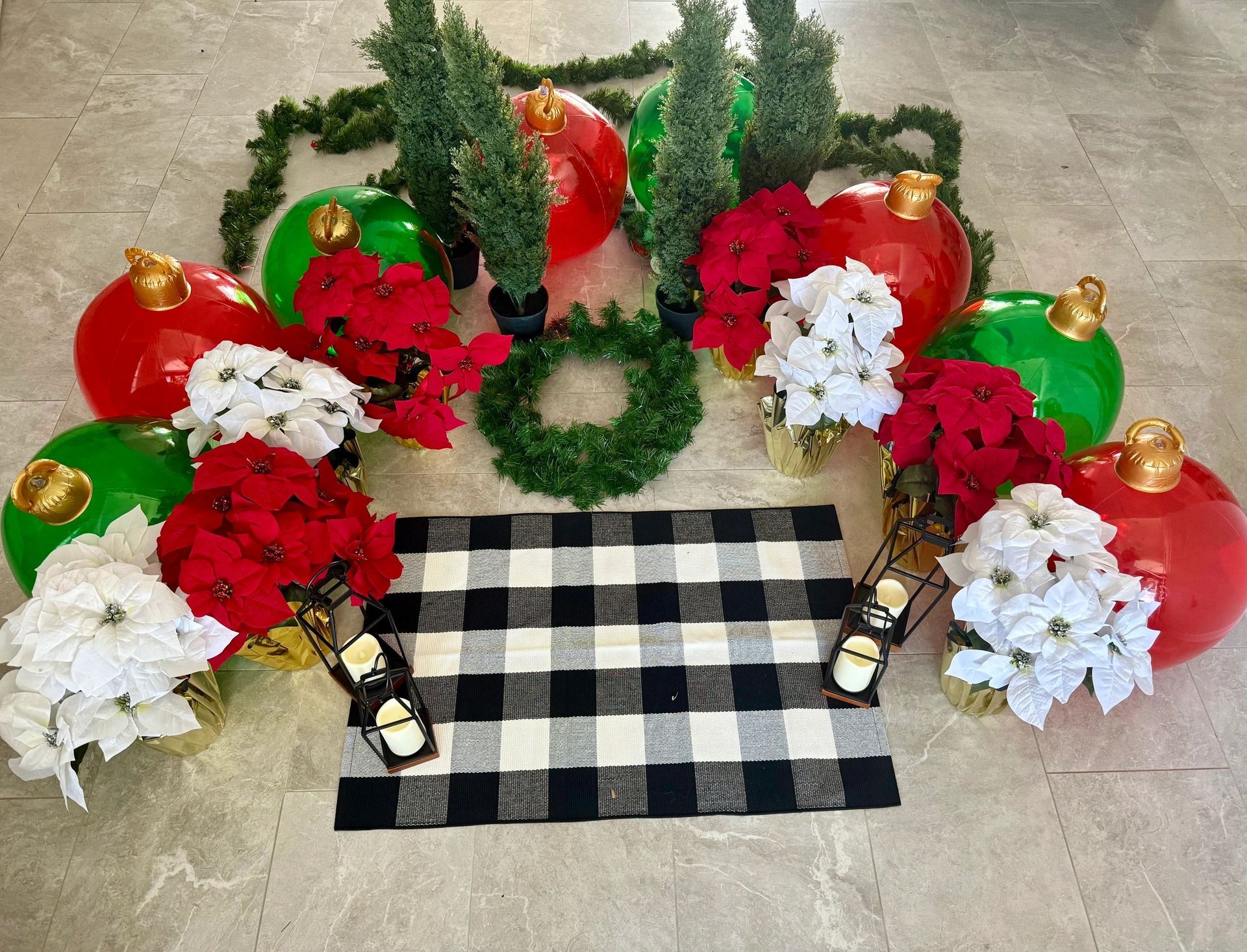 Christmas decorations featuring oversized ornaments, faux plants, and a plaid mat.