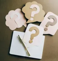 Notebook, pen, and paper cut-out question marks on a brown surface, suggesting a brainstorming session.