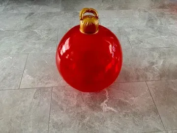 Large red Christmas ornament with gold cap and hook, on a gray tiled floor.