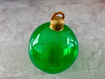 Large, green, shiny Christmas ornament on a tiled surface with gold top.