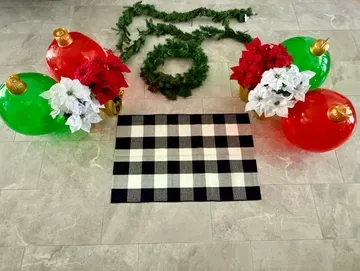 Christmas decor: red & green ornaments, poinsettias, wreath, garland, plaid rug on gray floor.