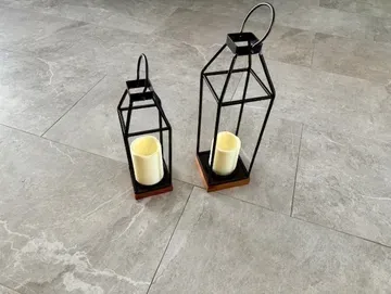 Two black metal lanterns with cream-colored candles on a gray marbled floor.