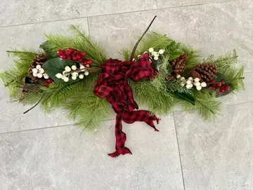 Christmas greenery with red plaid bow, berries, and pinecones on a light gray surface.