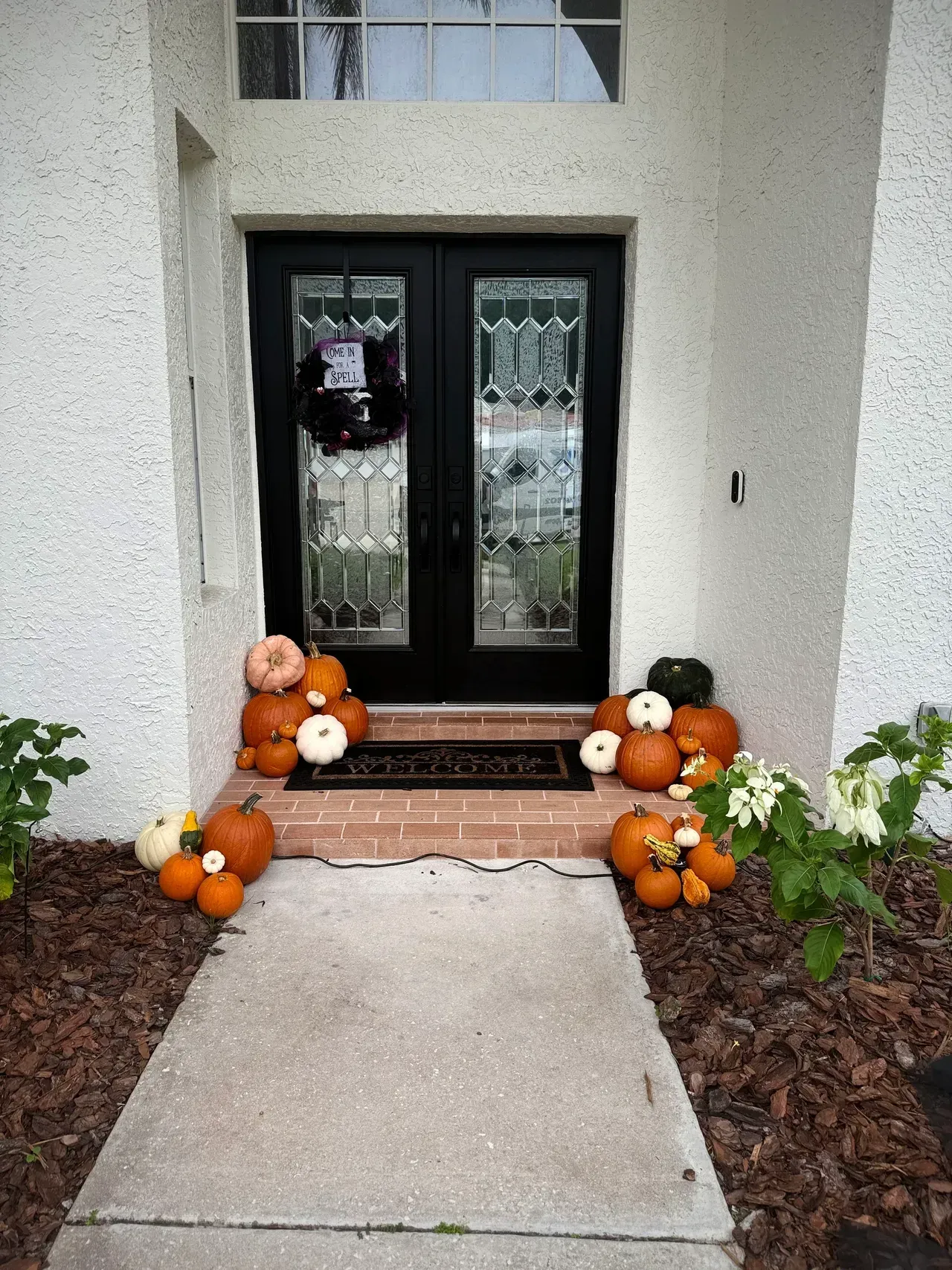 Double black front doors decorated with pumpkins and a wreath.
