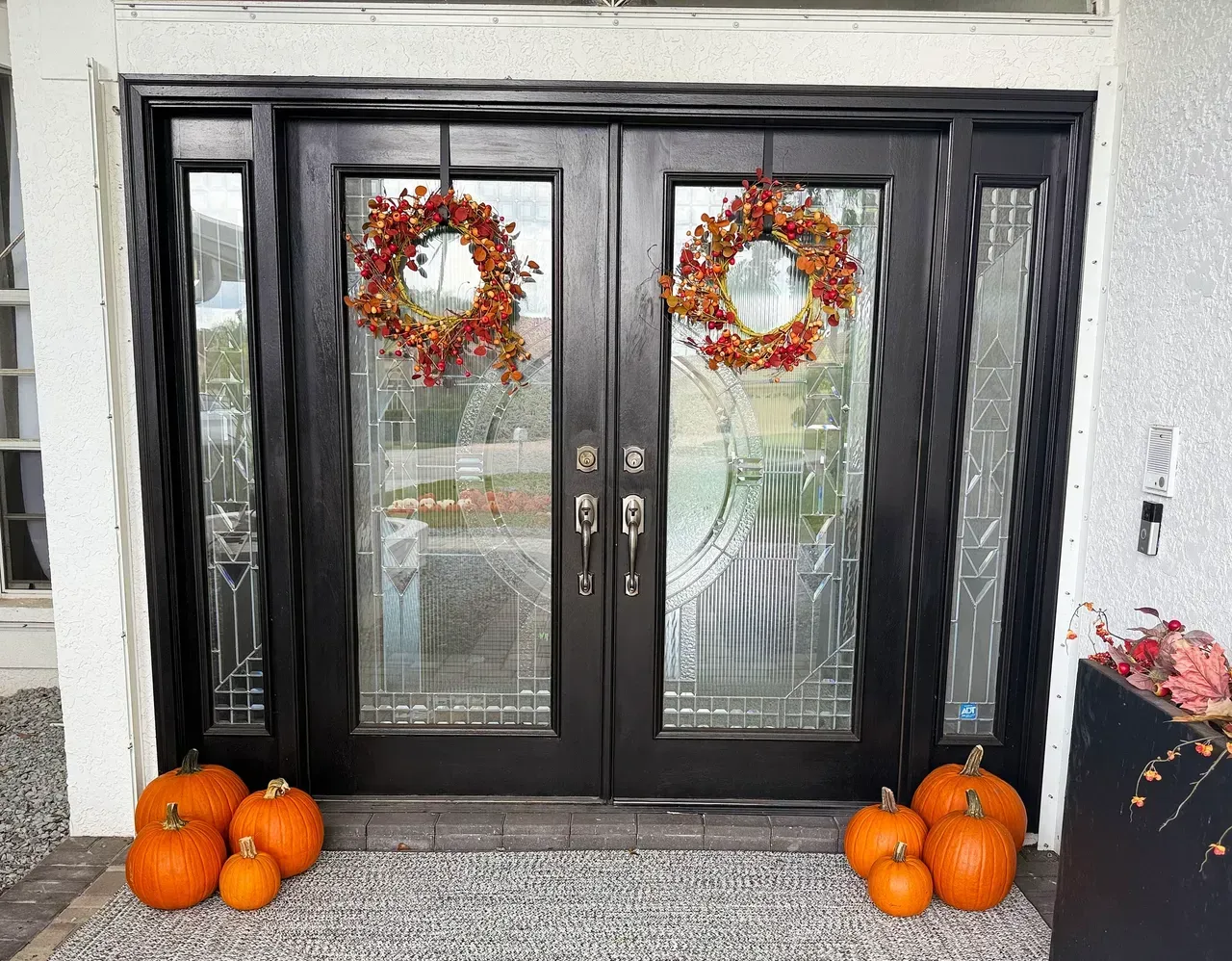 Double black front doors decorated for fall with wreaths and pumpkins.