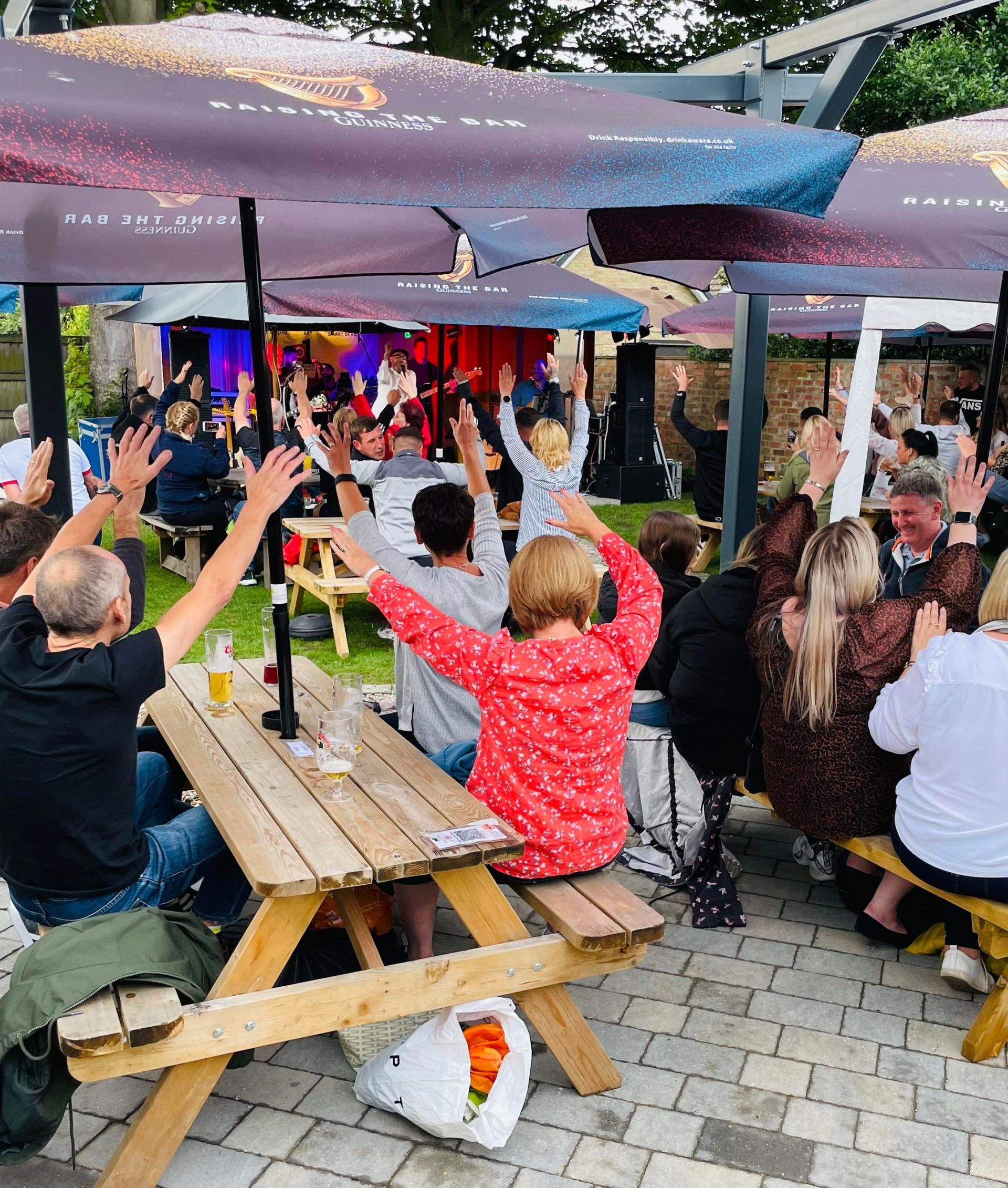 A group of people are sitting at a picnic table with their arms in the air.