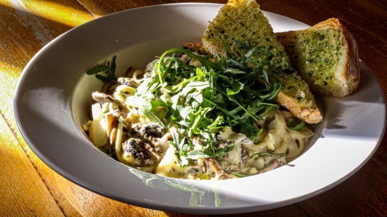 A bowl of pasta with garlic bread on a wooden table.