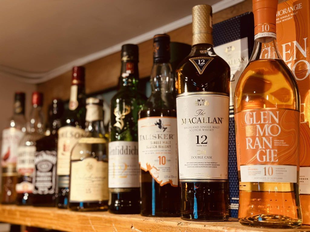 A row of bottles of alcohol are lined up on a wooden shelf.