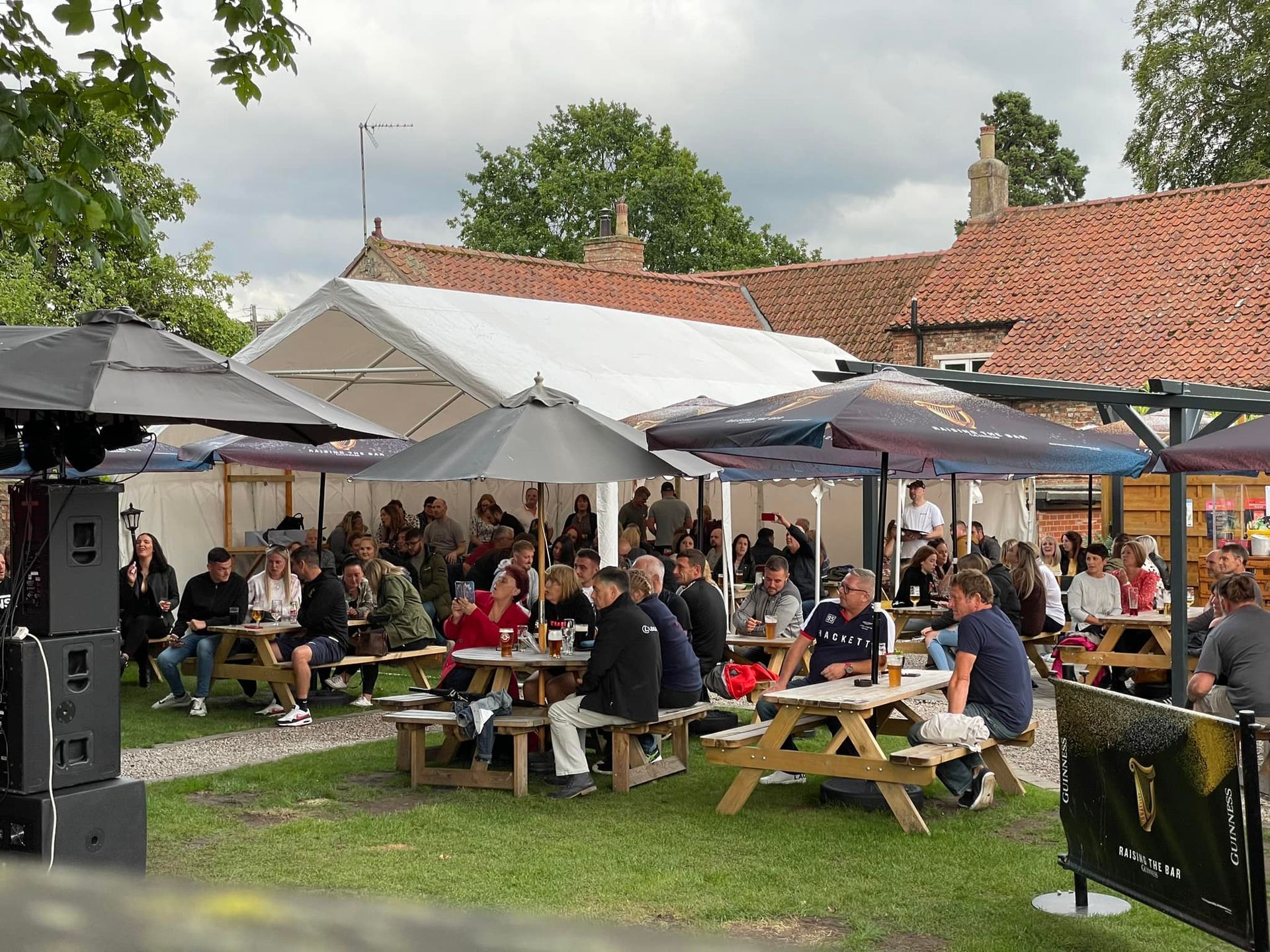A group of people are sitting at picnic tables under umbrellas in a park.