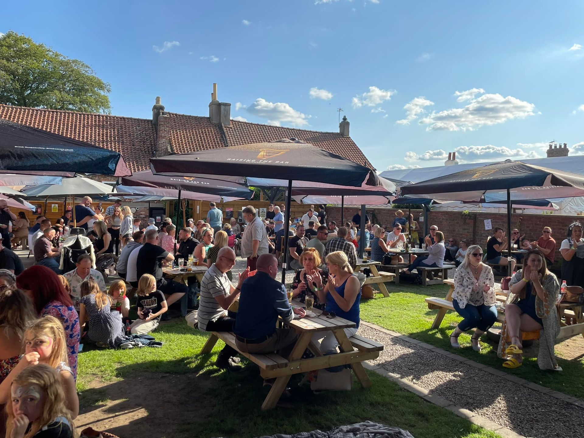 A large group of people are sitting at picnic tables in a park.
