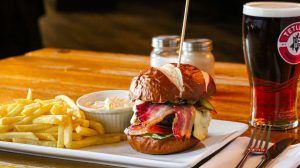 A hamburger and french fries are on a plate next to a glass of beer.