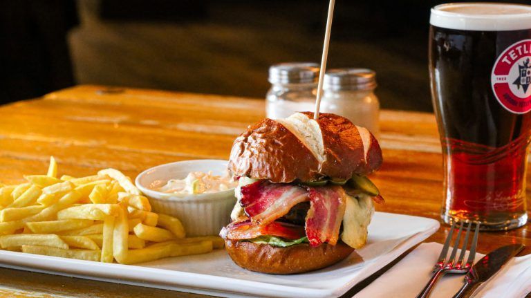 A hamburger and french fries are on a plate on a table next to a glass of beer.