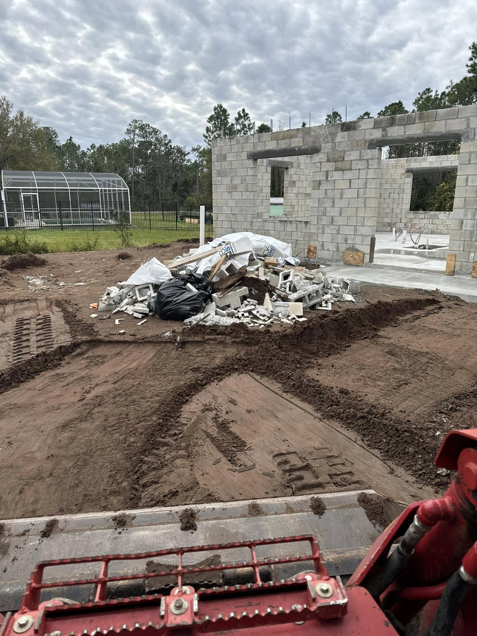 Construction site with a pile of debris and cinder block structure. Earthmover in foreground, overcast sky.